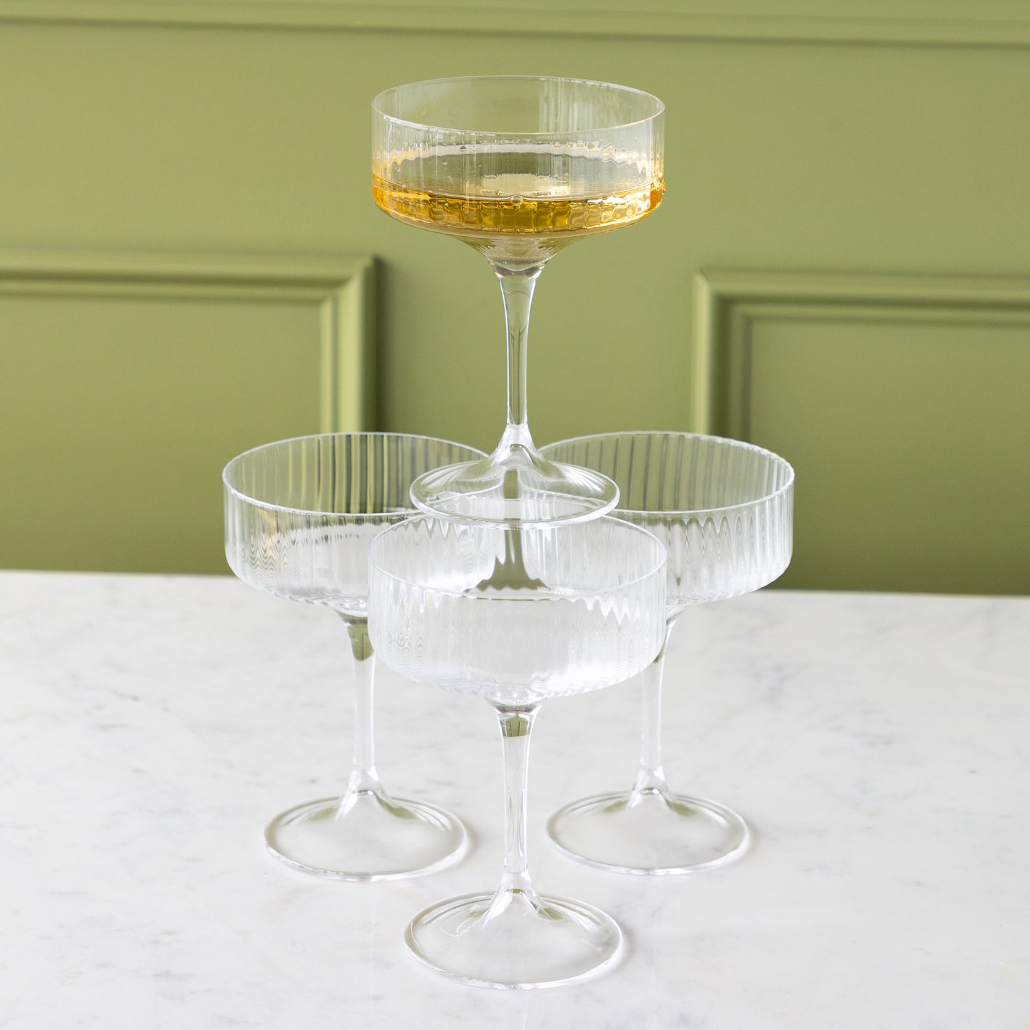 Four Fluted Textured Coupe Glasses; three on the table and one stacked on top filled with champagne.