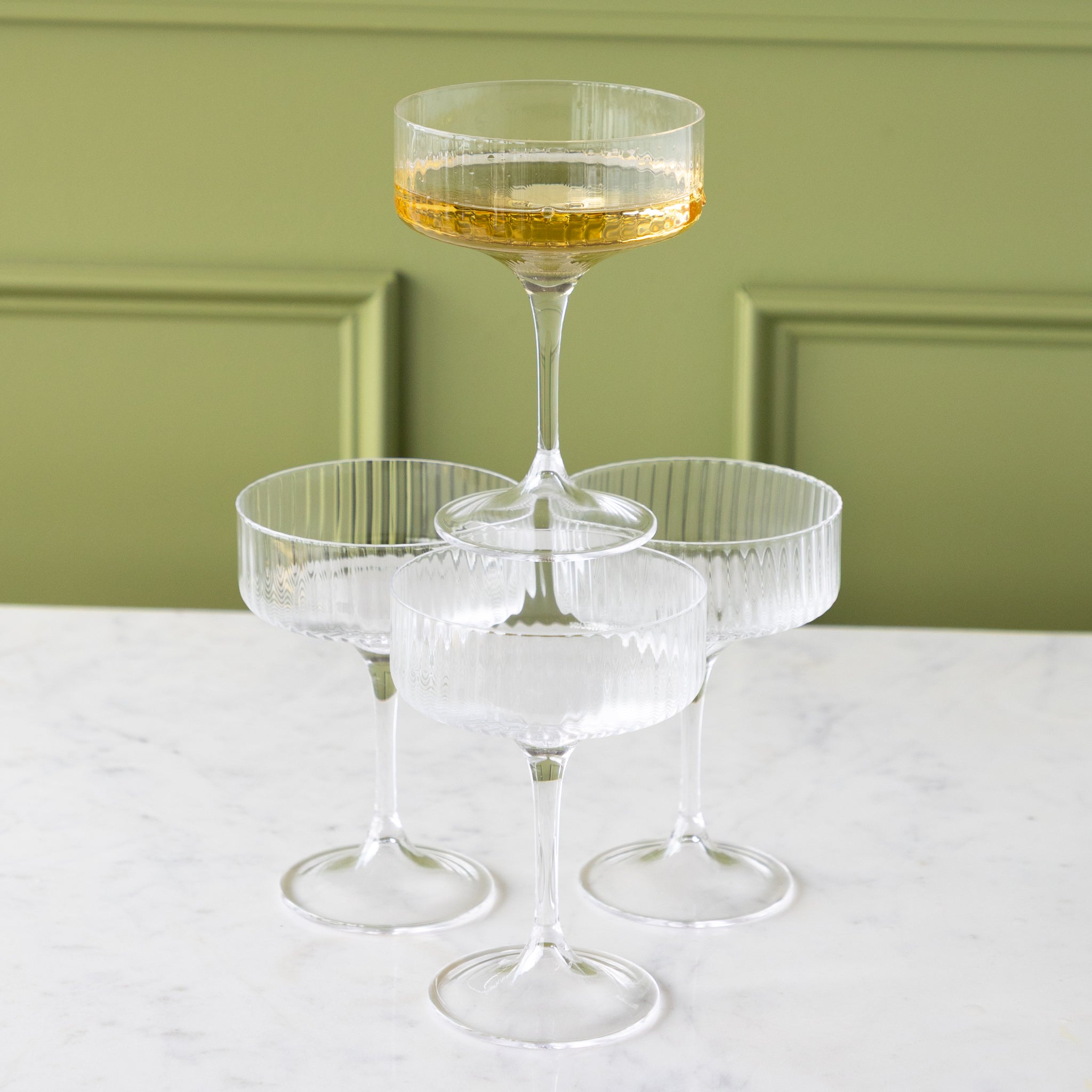 Four Fluted Textured Coupe Glasses; three on the table and one stacked on top filled with champagne.