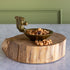 A decorative bowl with a squirrel-shaped handle, filled with cashews and dried fruit pieces, displayed on a rustic round wooden slice stand against a green paneled wall and light marble surface.