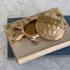 A brass turtle-shaped keepsake box with an embossed lid, resting on top of vintage floral books on a marble surface.