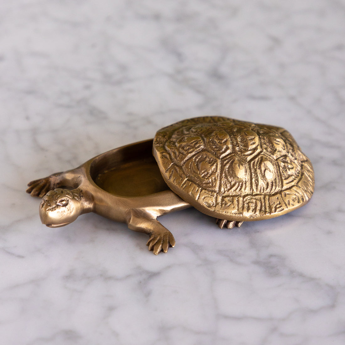 A brass turtle-shaped container with an open shell, resting on a white marble surface.