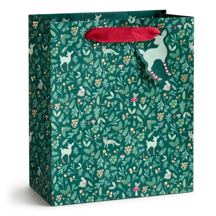 A green gift bag with a festive woodland pattern of deer, rabbits, and small mushrooms, featuring a red ribbon handle and a hanging reindeer tag.
