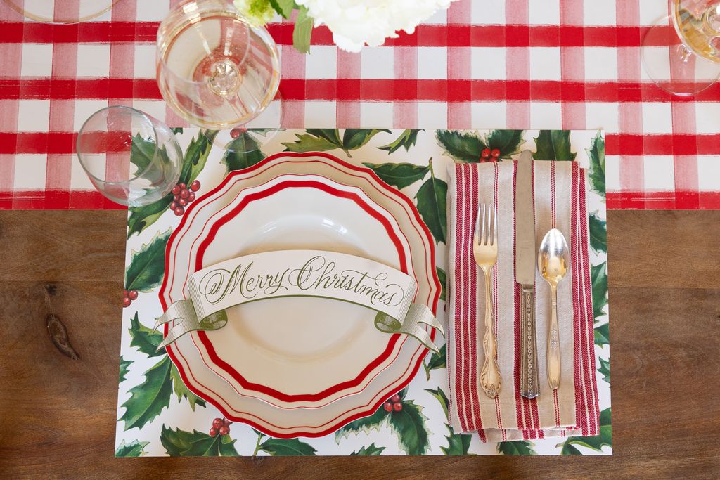 Christmas-themed place setting with a decorative plate, cutlery, and napkin on a red and white checkered tablecloth.