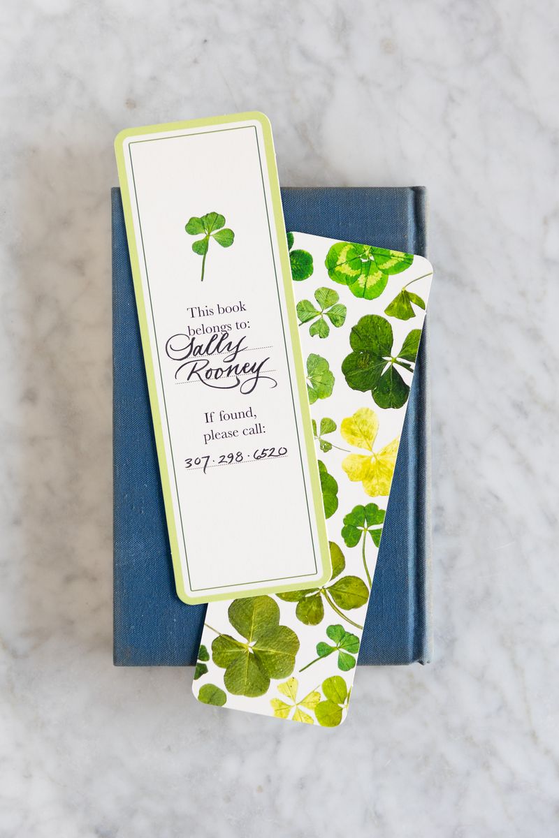 Book with a bookmark featuring a four-leaf clover design on a marble surface