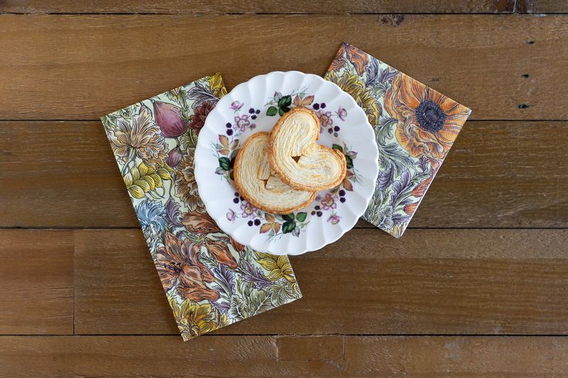 Decorative paper napkins with floral design on a wooden surface, featuring a plate with cookies.