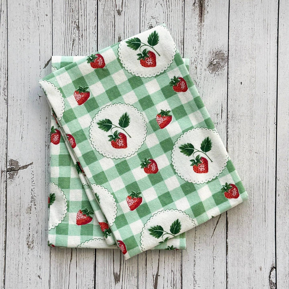 Two green checkered towels with strawberry pattern on a wooden surface.