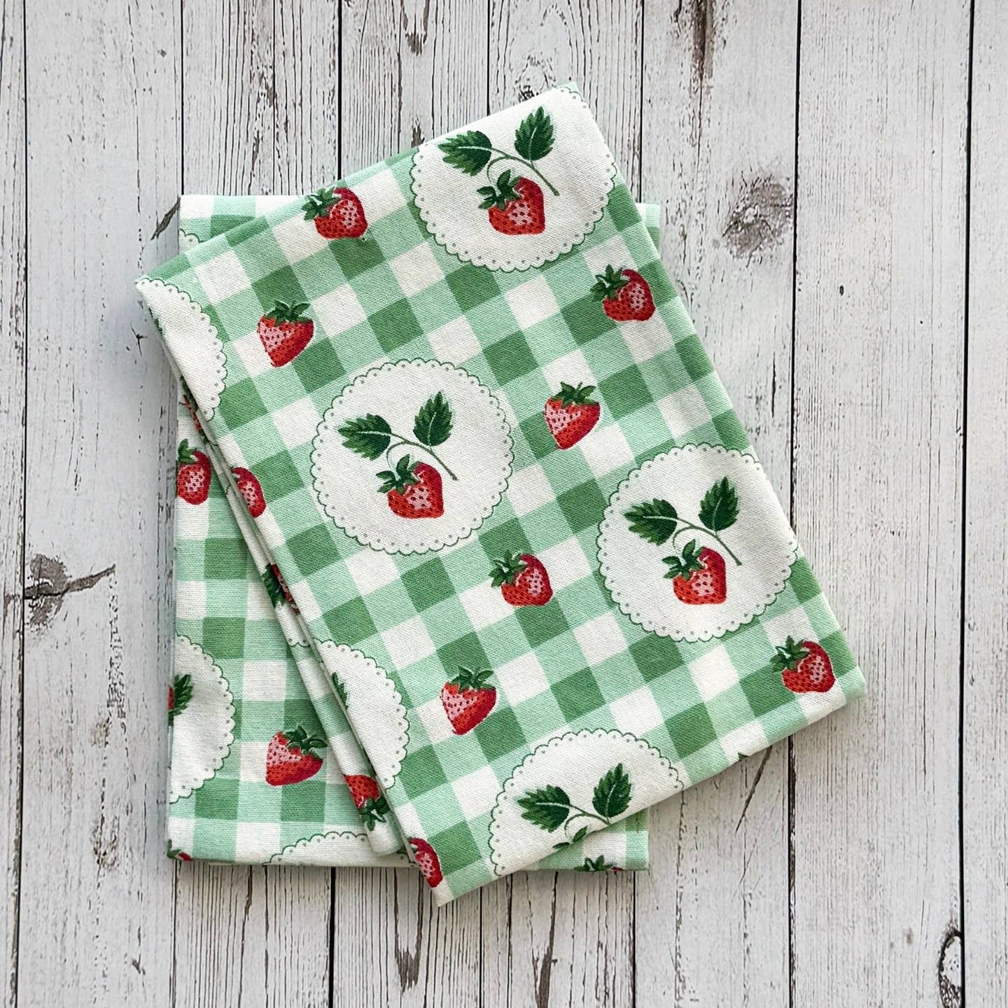 Two green checkered towels with strawberry pattern on a wooden surface.