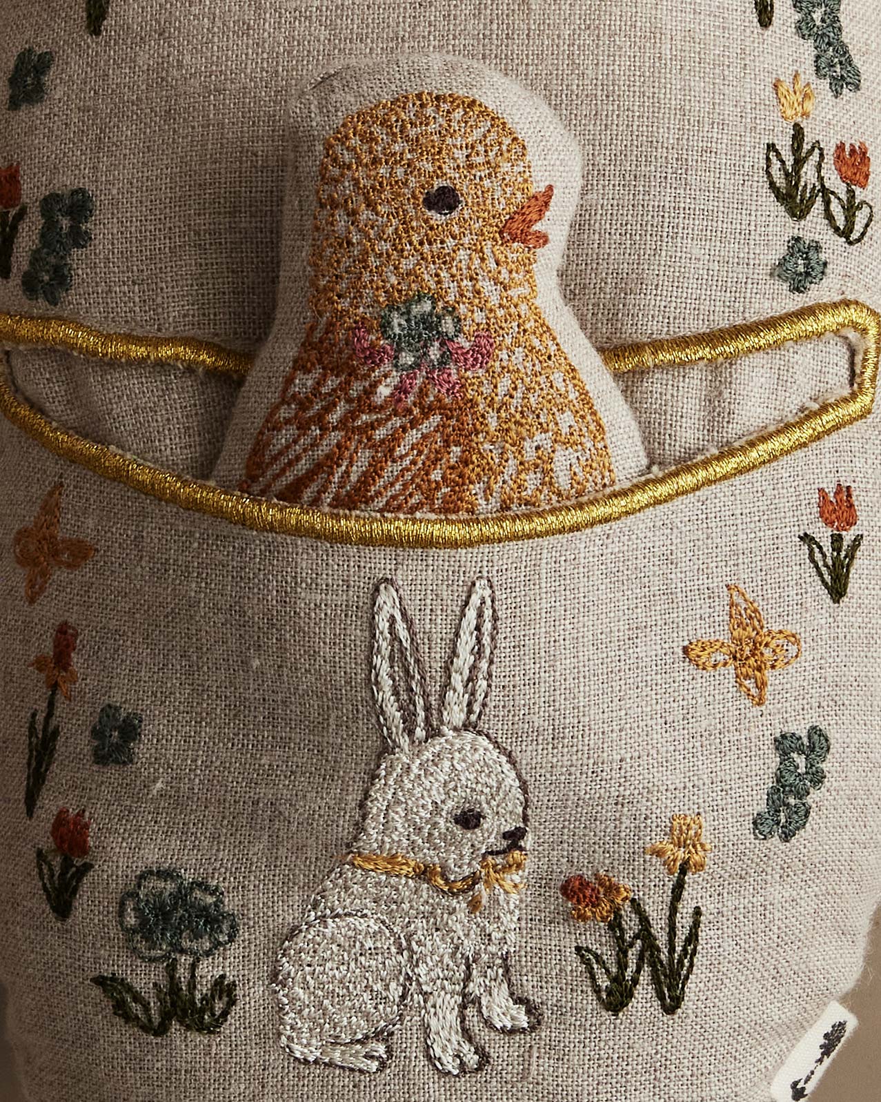Embroidered fabric with a chick and rabbit design on a textured background.