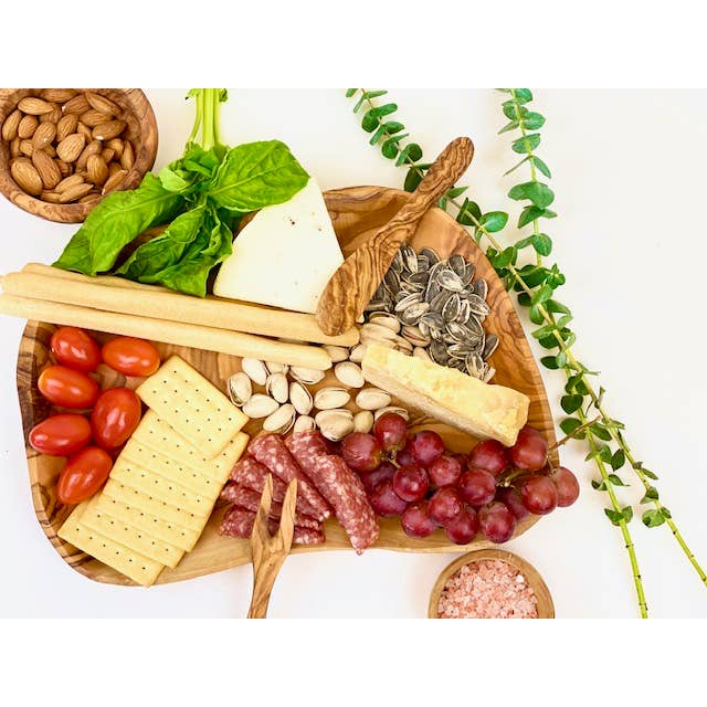 A serving board made of olive wood with charcuterie displayed on it. 