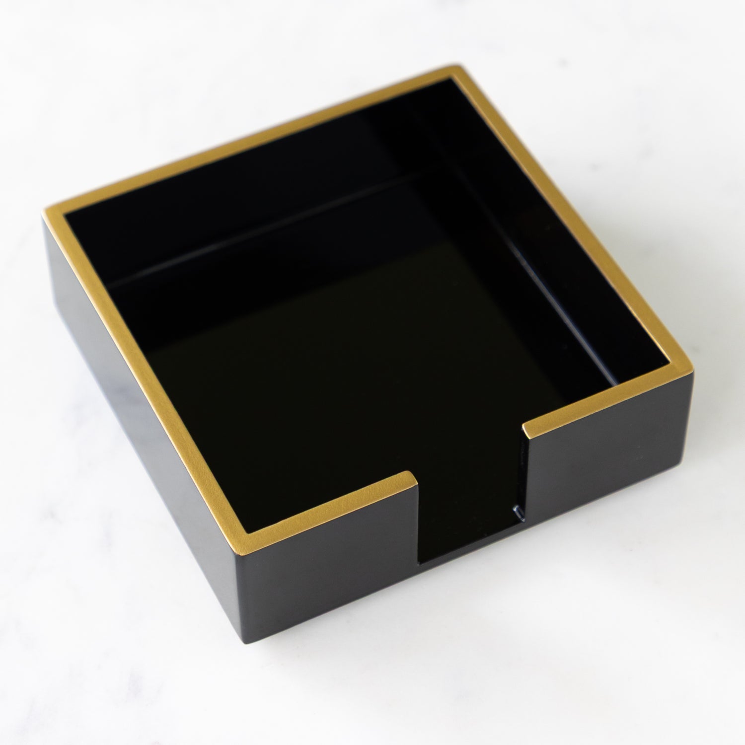 Black Beverage Napkin Holder with Gold Trim on a marble table.
