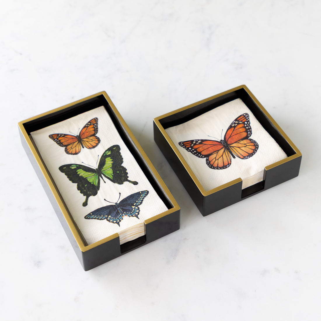 Black Napkin Holders with Gold Trim in a cocktail and guest size with Hester &amp; Cook Butterfly Napkins in them.