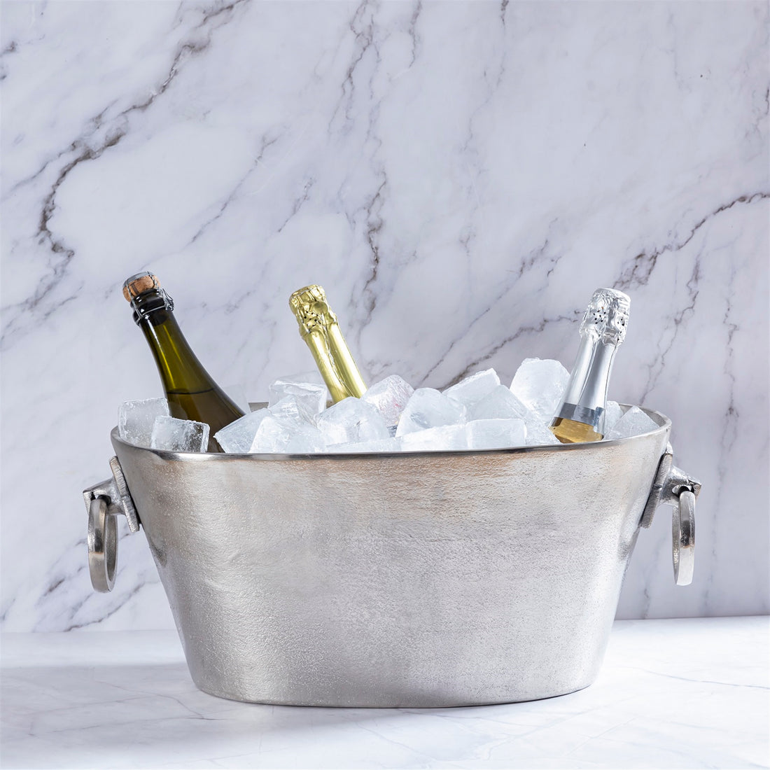 Metal ice bucket with three bottles of champagne on a marble background.