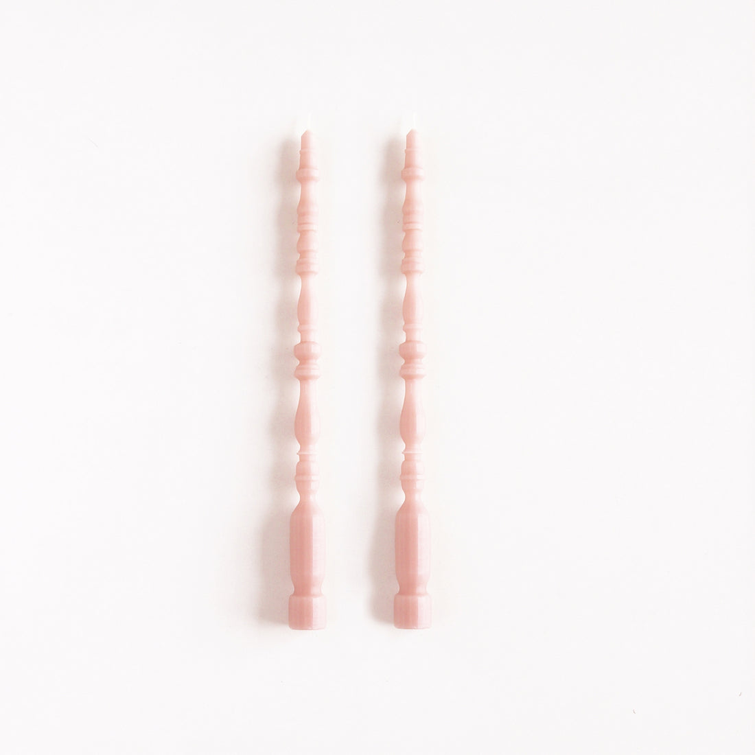 2 taper candles shaped like table spindle legs in rosewater. 
