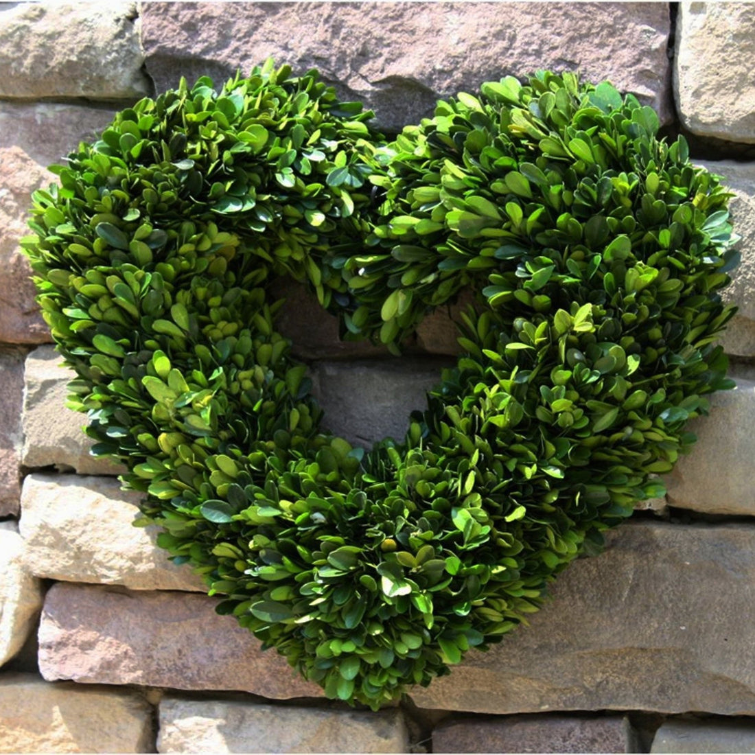 Boxwood Heart Wreath hanging on a stone wall.