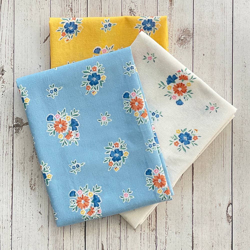 Three folded fabric swatches with floral patterns on a wooden surface