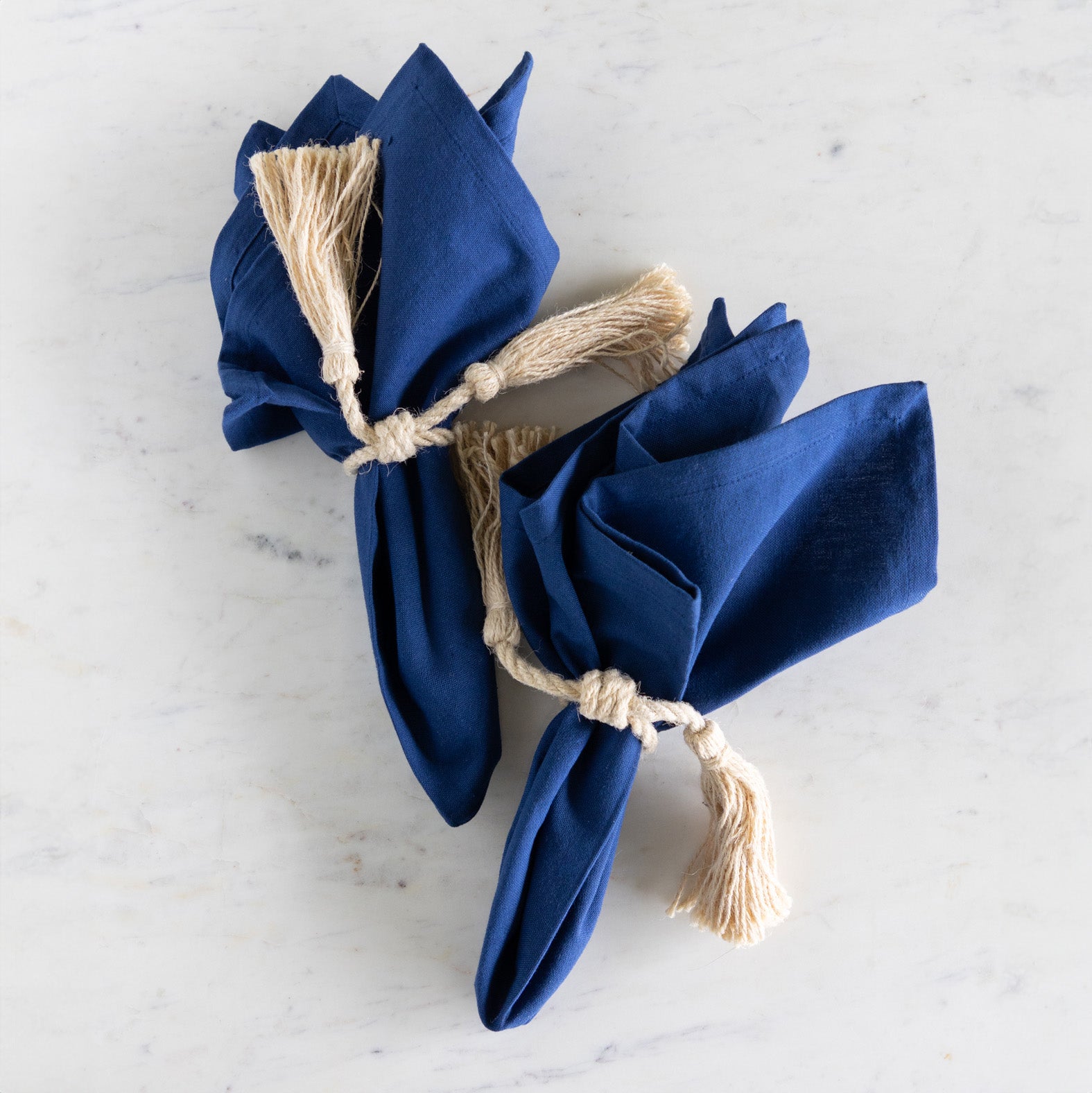 Two blue napkins tied with twine on a light gray surface.
