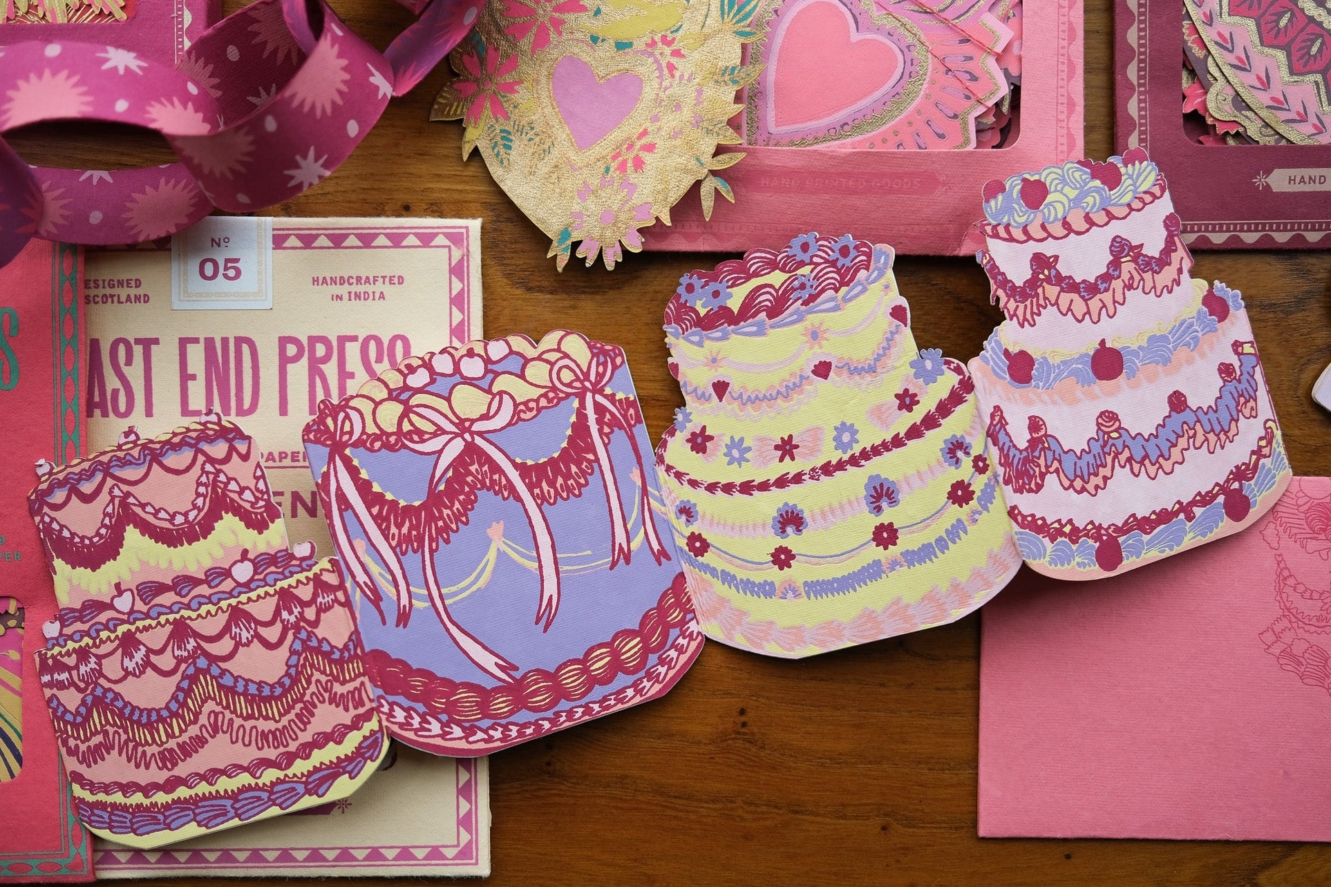 Colorful card designs featuring cakes and bows on a wooden surface.