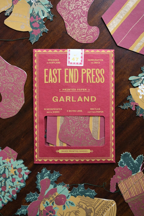 East End Press Garland printed paper box displayed on a dark wood surface, surrounded by decorative paper cutouts in pink, gold, and teal.