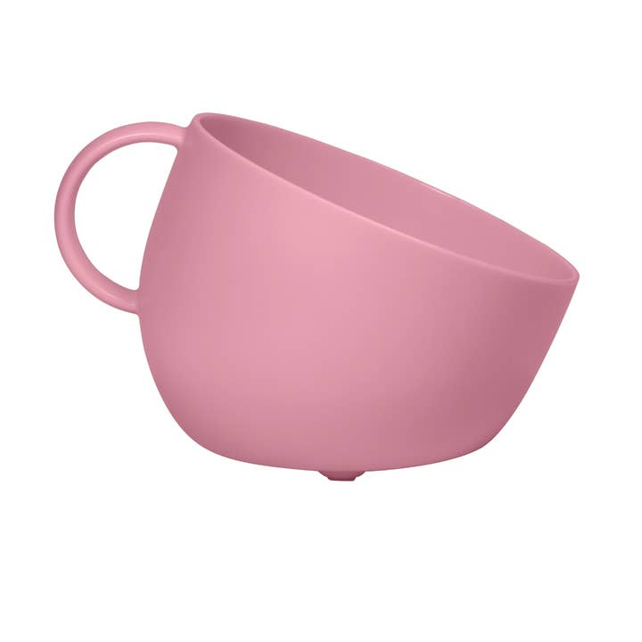 A matte pink mug shaped dog bowl with a matching red handle, shown at an angle on a plain white background.