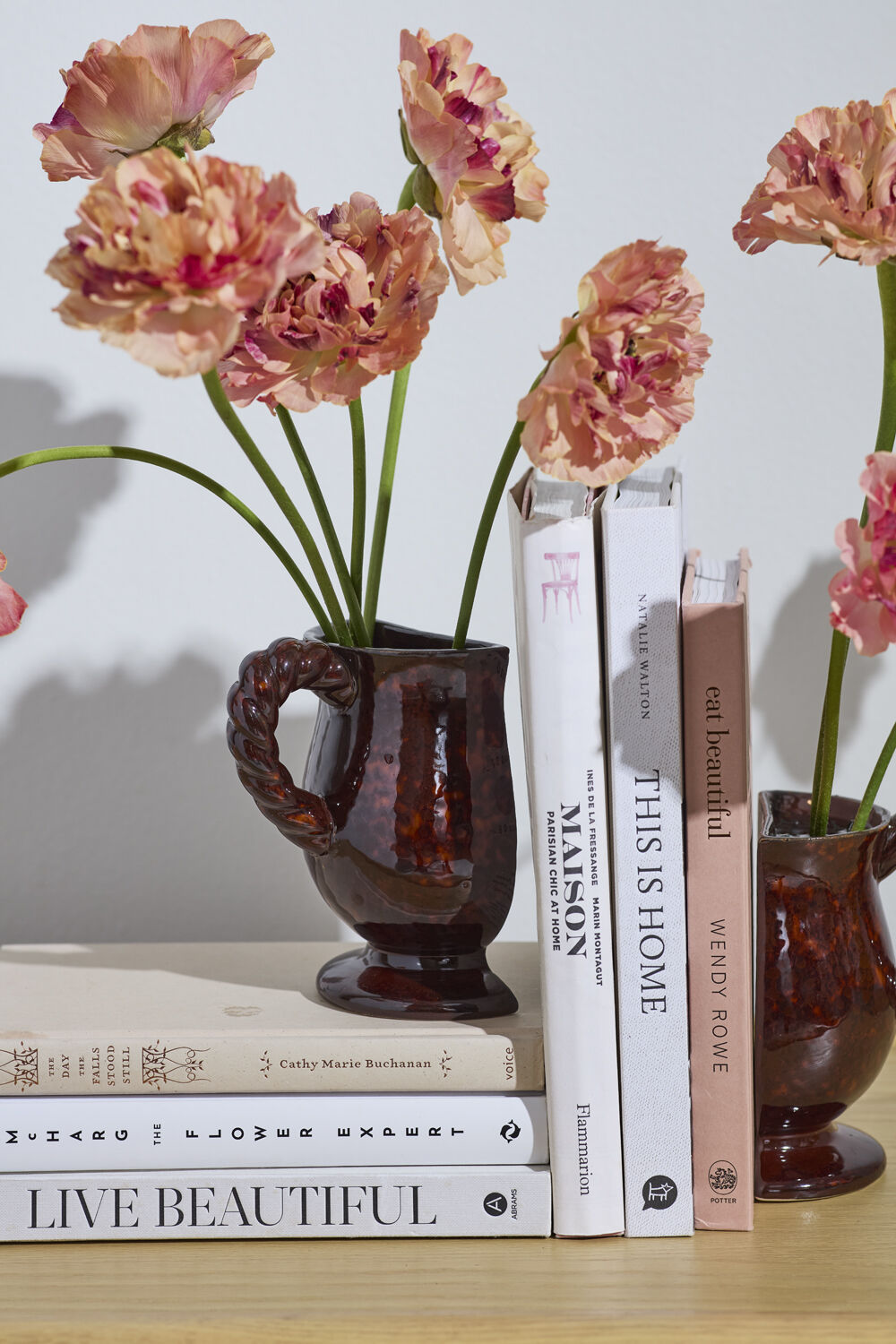 Decorative arrangement with pink flowers in brown vase-shaped book ends on books