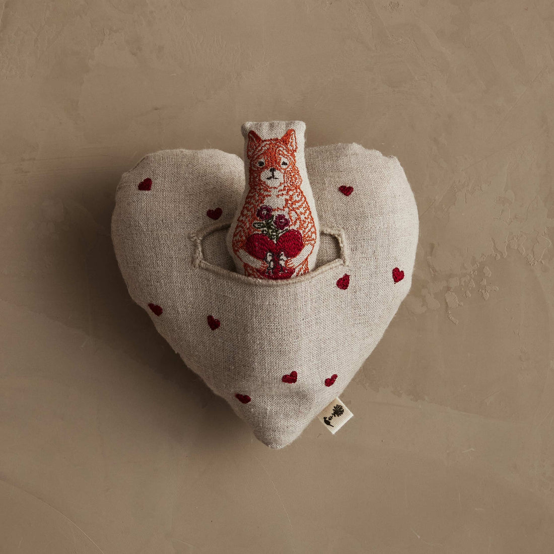 Heart-shaped pillow with a fox plush toy and red hearts on a beige background.