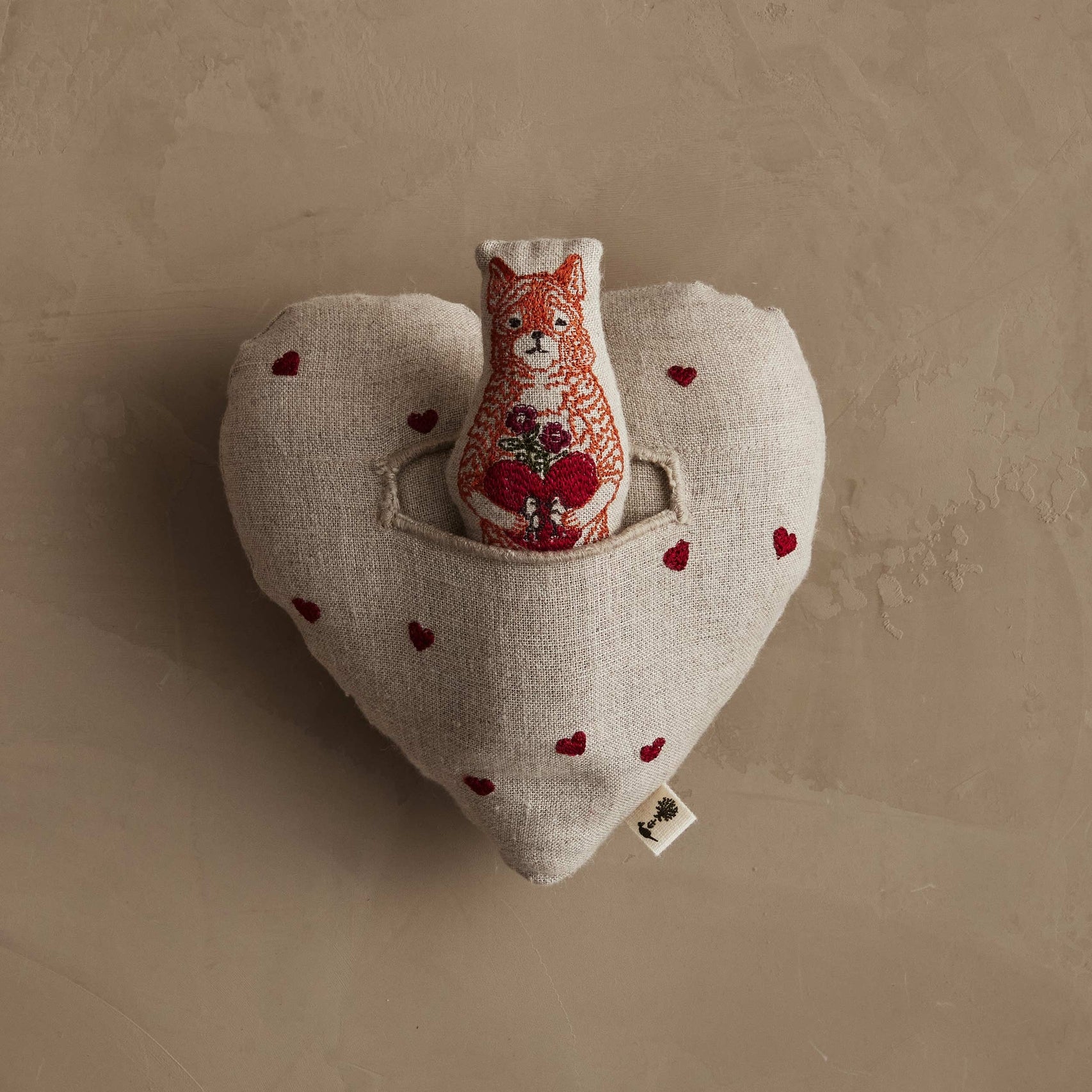 Heart-shaped pillow with a fox plush toy and red hearts on a beige background.