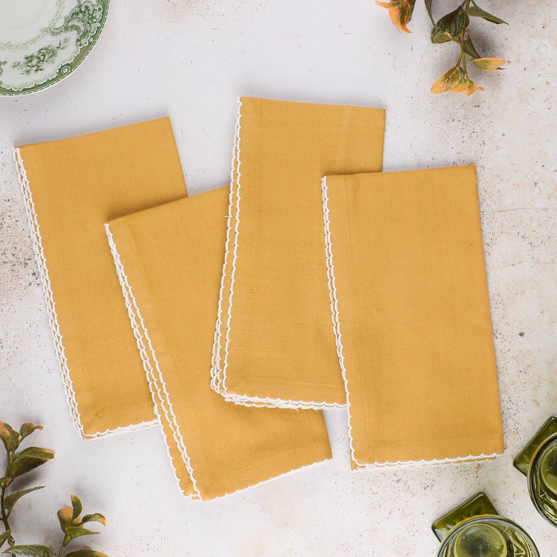 Set of mustard yellow napkins with white lace trim on a light surface.