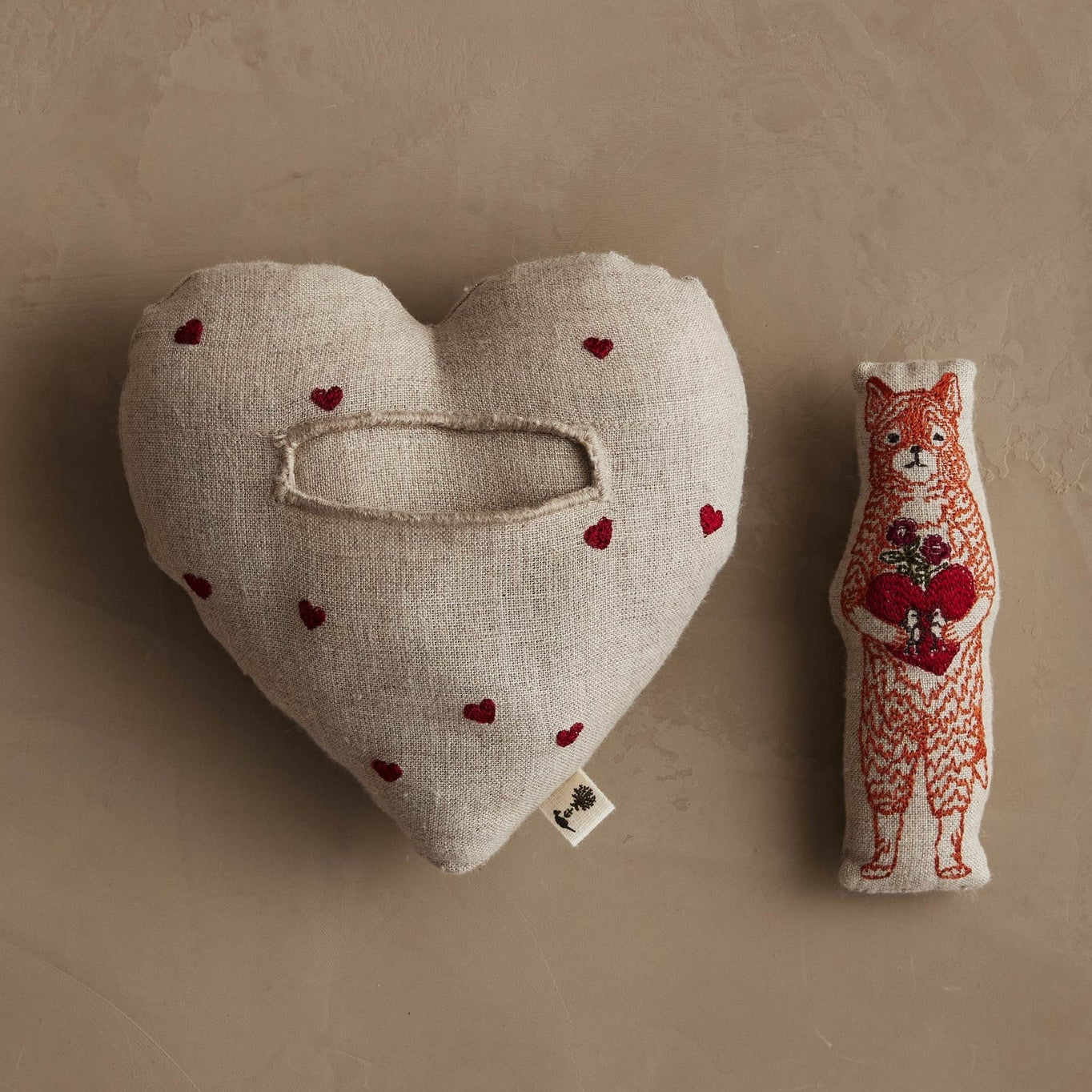 Heart-shaped pillow with red heart patterns and a fox plush toy on a beige background.