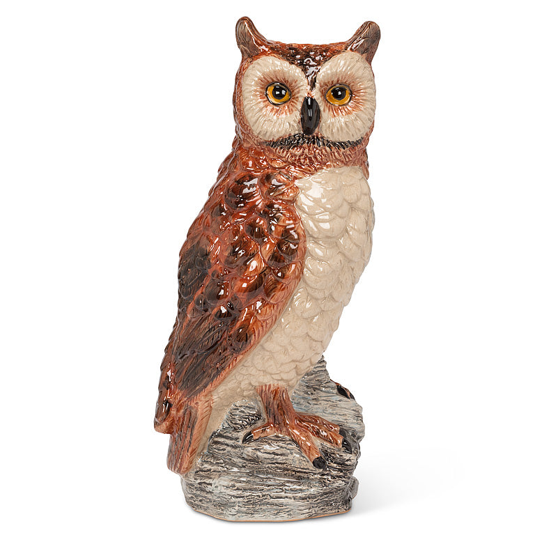 A ceramic owl figurine perched on a textured tree branch base, featuring brown and cream feathers with yellow eyes, on a white background.