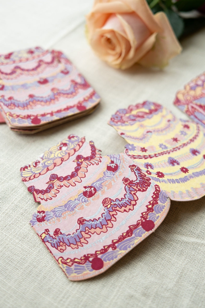 Decorative greeting card with cake design on a textured surface with a rose in the background.