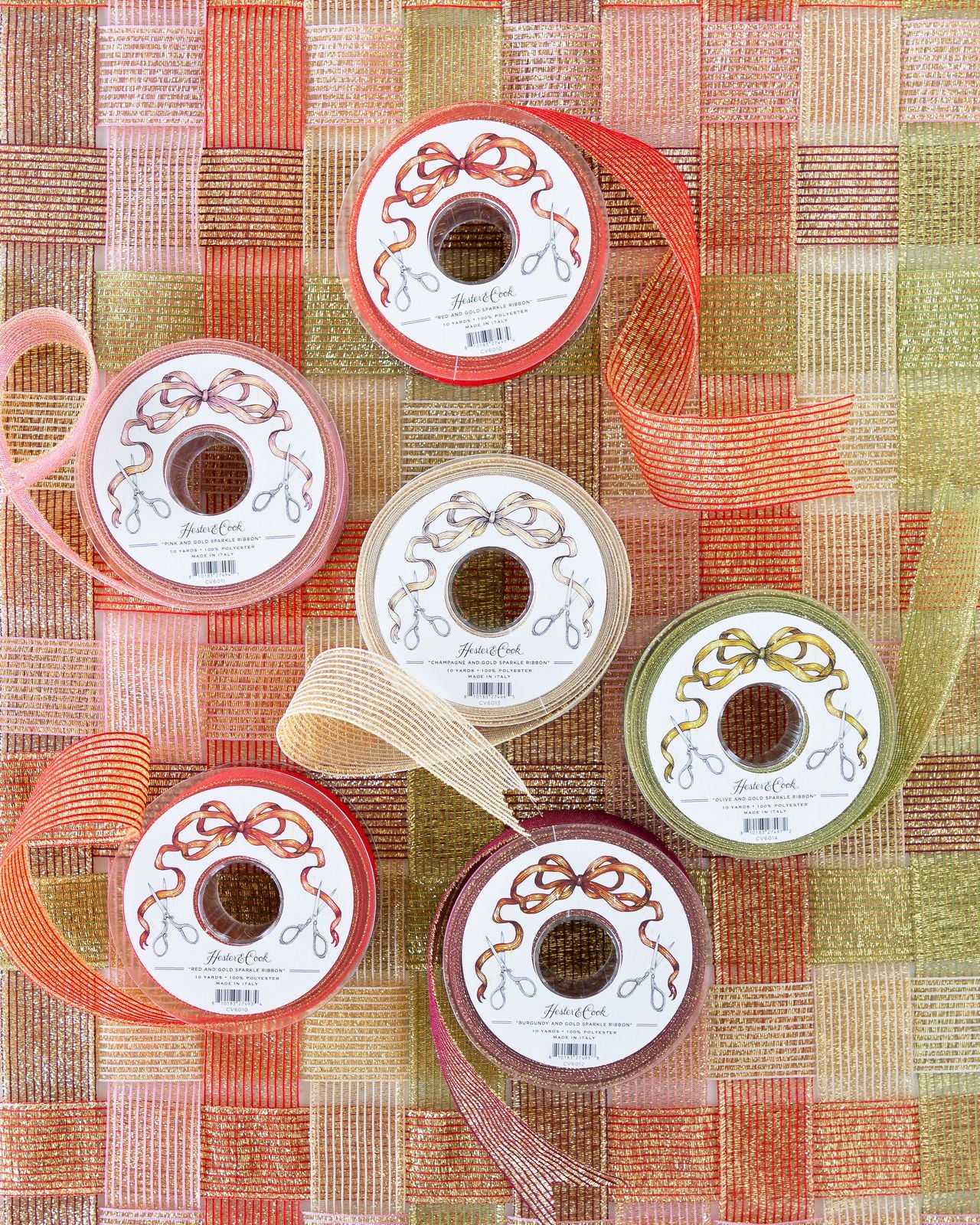 Several spools of sparkly ribbon in various colors unraveled on a surface of woven sparkle ribbon. 
