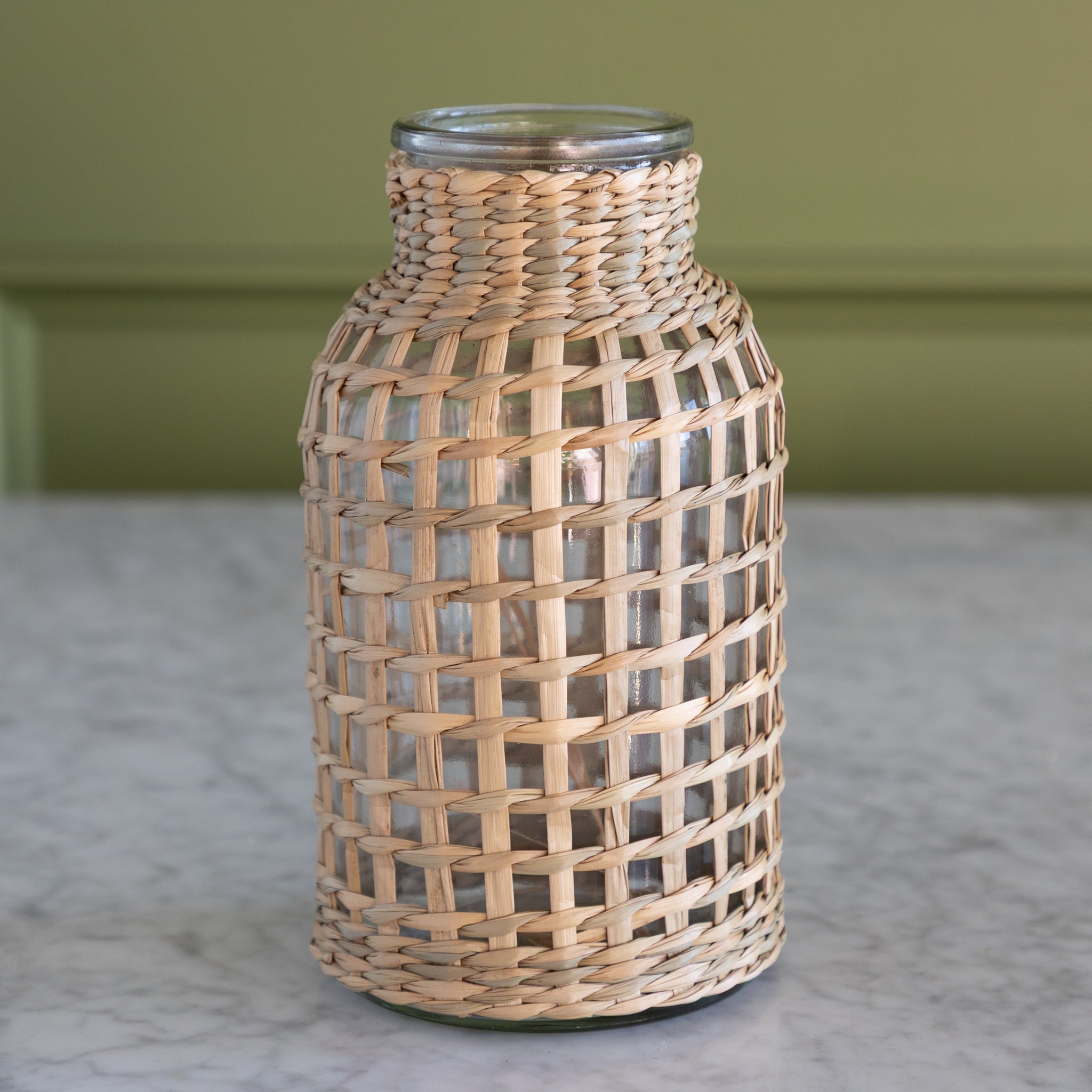 Glass bottle with woven rattan cover on a marble surface.