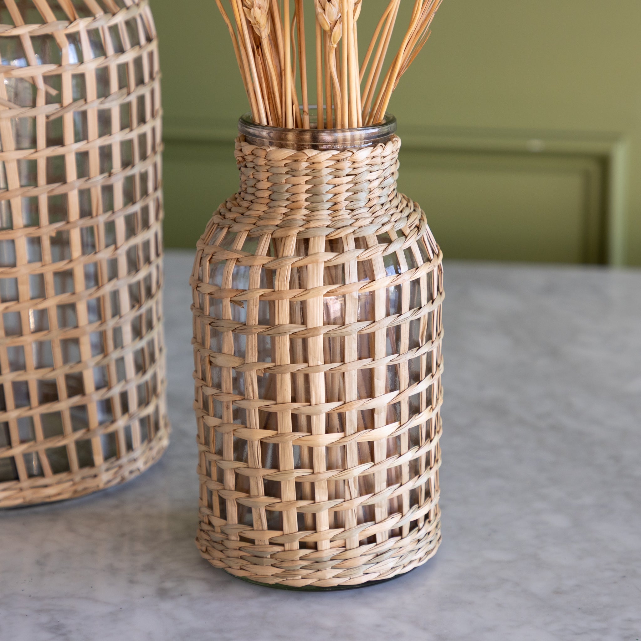 A small Rattan Wrapped Glass Vase on a marble table.