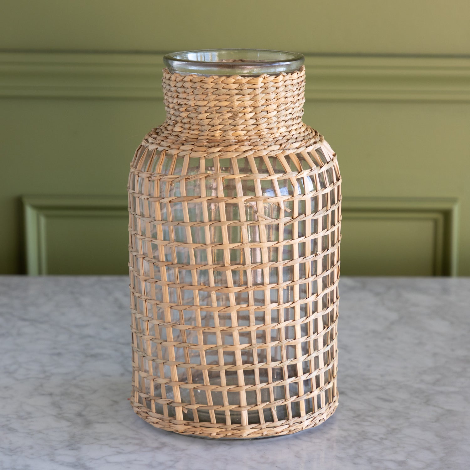 Woven rattan vase on a marble surface with a green wall background.
