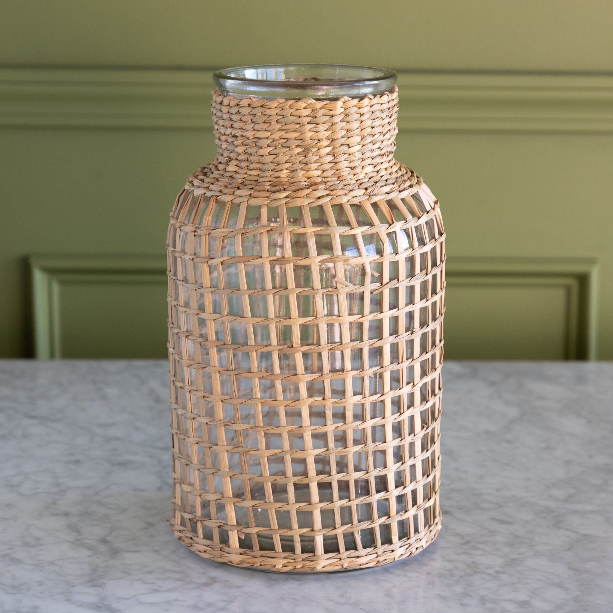 Woven rattan vase on a marble surface with a green wall background.