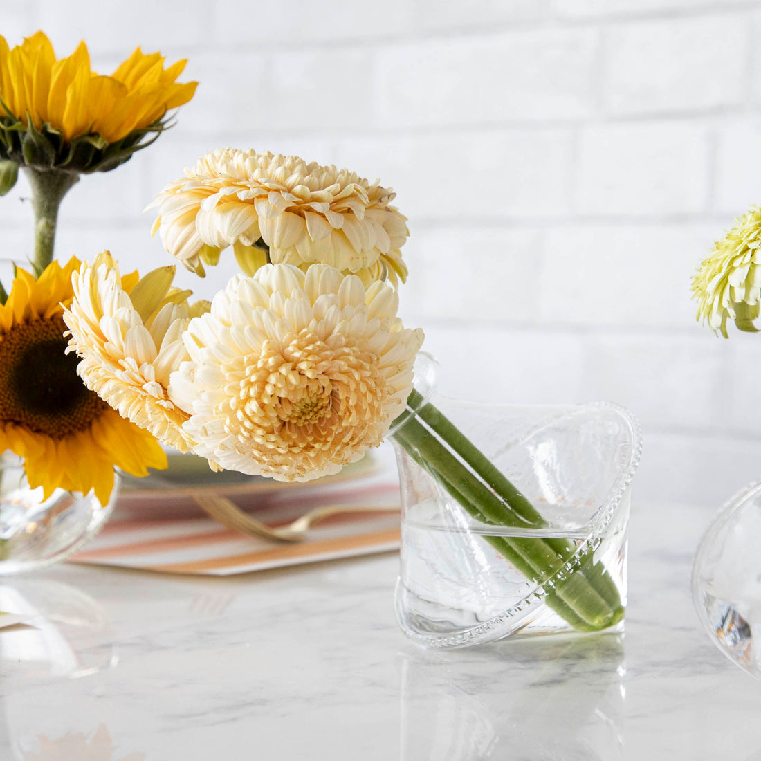 Three Qualia Mouth Blown Clear Vases - Exclusively at Hester &amp; Cook with small bouquets of favorite flowers sitting on a table.