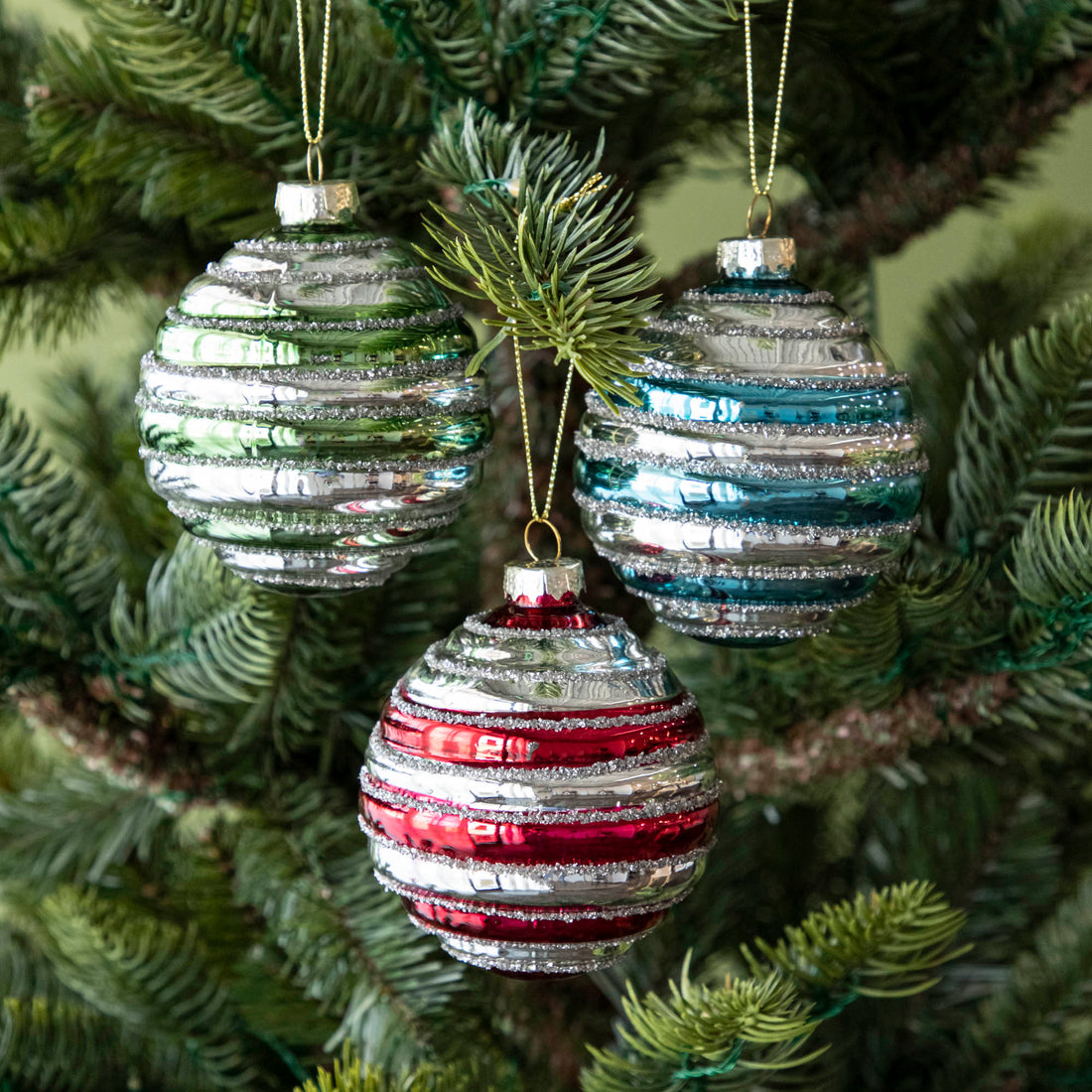 Three Glass Silver Stripe Ball Ornaments in silver with red, green or blue stripes, hanging on a tree by a gold string.