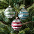 Three Glass Silver Stripe Ball Ornaments in silver with red, green or blue stripes, hanging on a tree by a gold string.