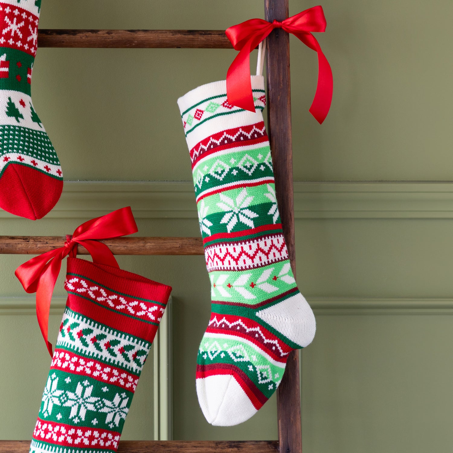 Decorative Christmas stocking with snowflakes on a wooden ladder against a green wall.