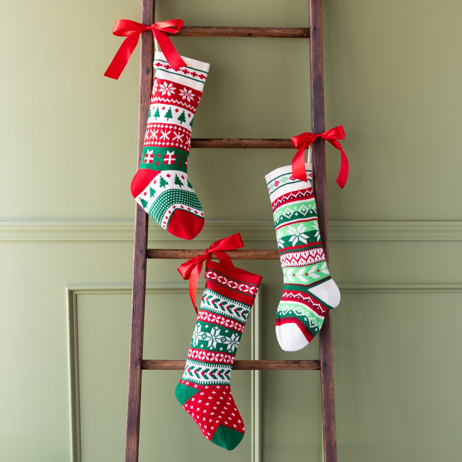 Decorative Christmas stockings with red bows on a wooden ladder against a green wall.