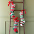 Decorative Christmas stockings with red bows on a wooden ladder against a green wall.