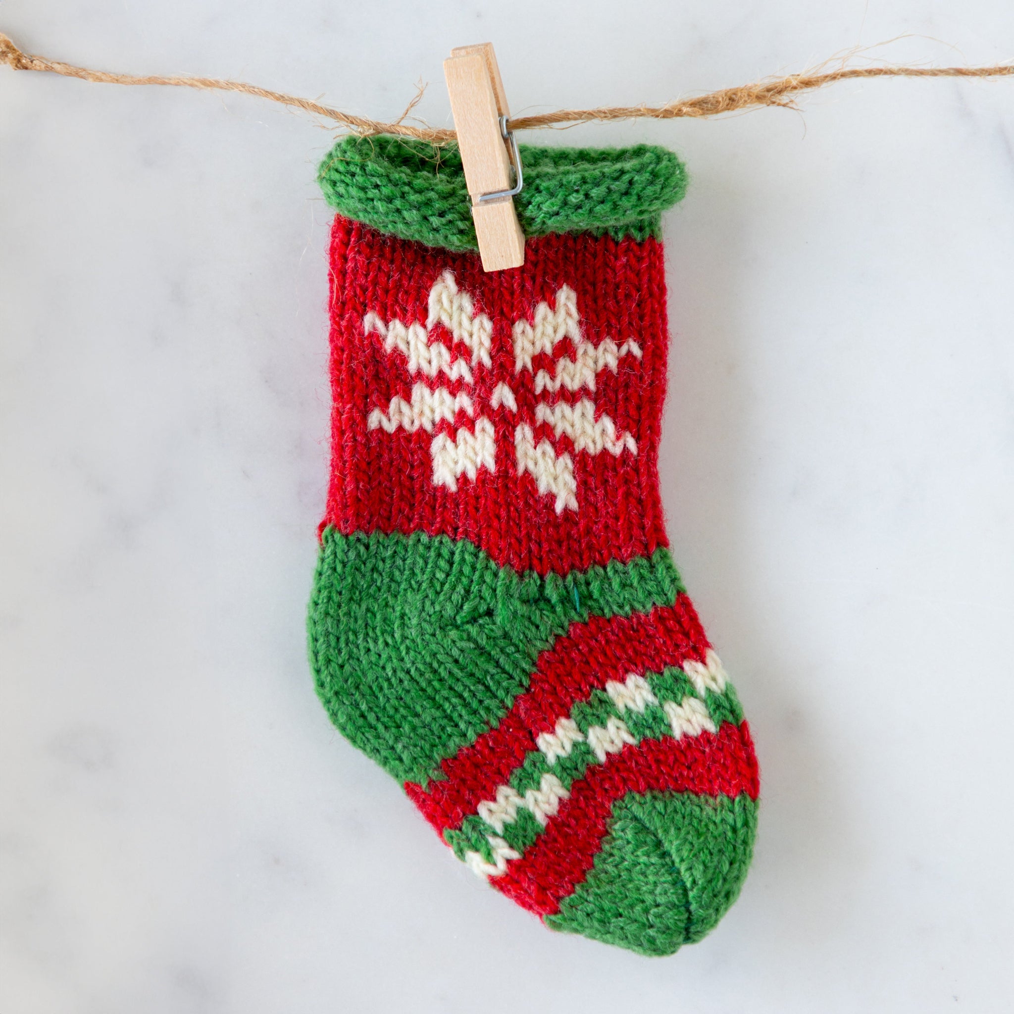 Knitted Christmas stocking with green top and red body, hanging on a string.