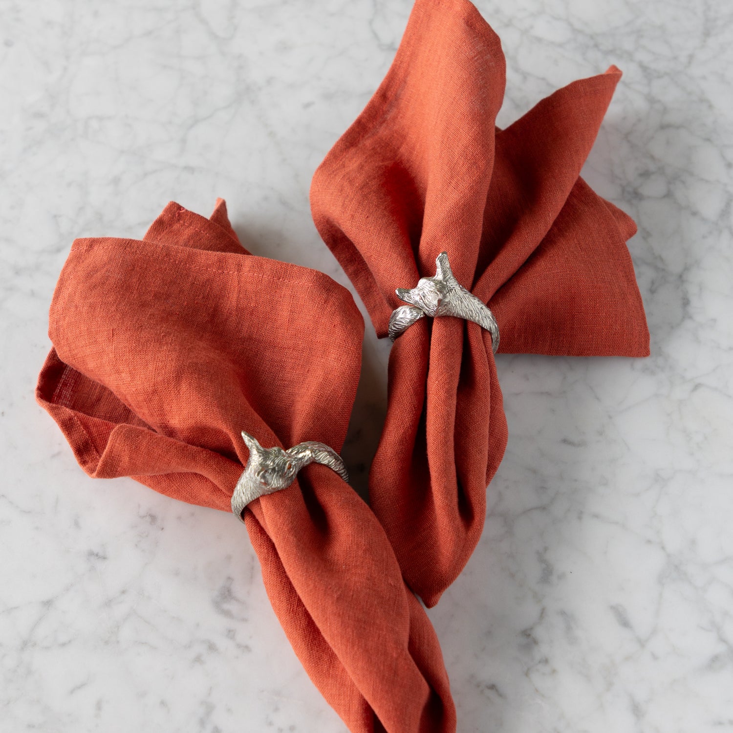 Two orange napkins with fox napkin rings on a marble surface.