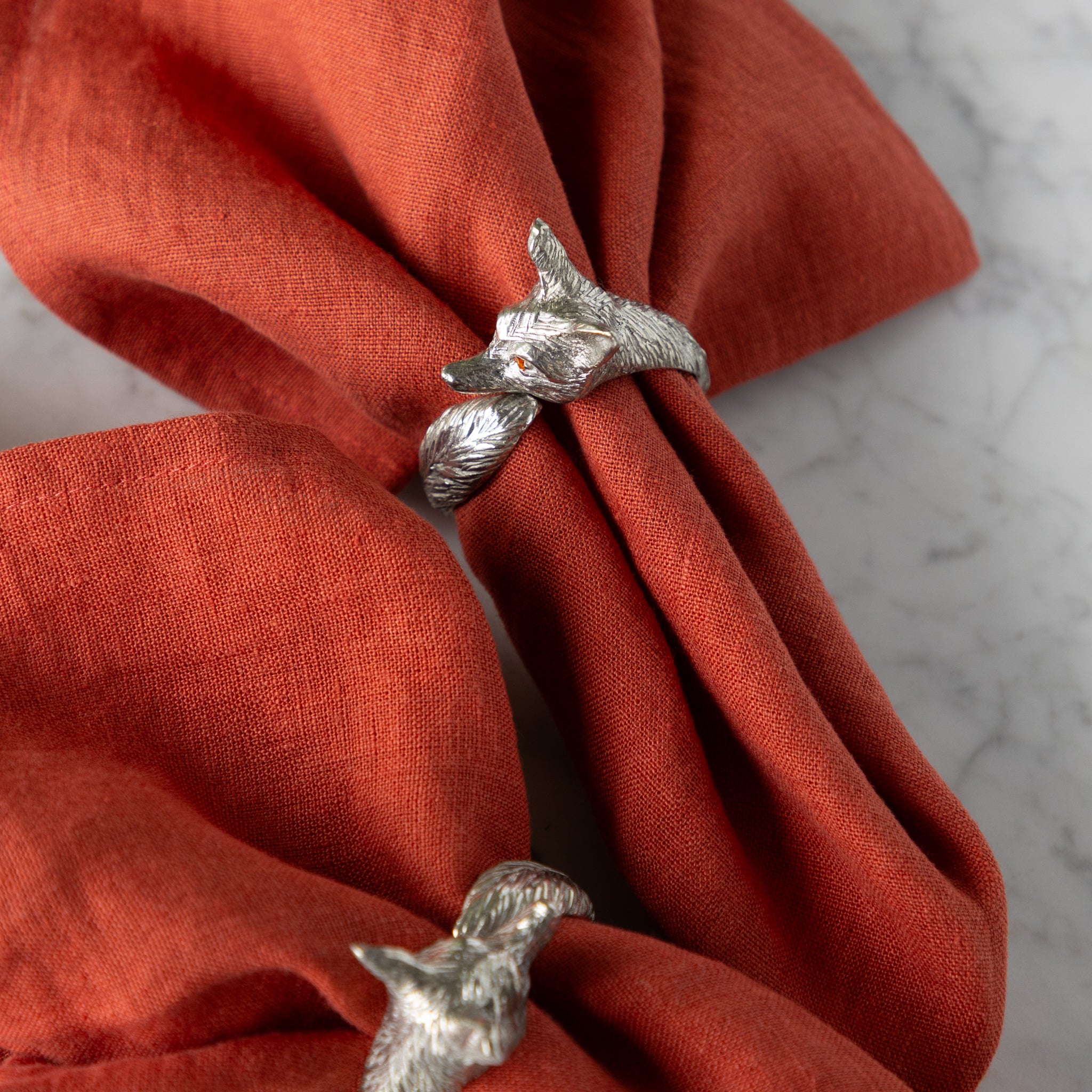 Silver fox-shaped napkin rings on orange napkins.