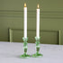 Two white candles in green candlesticks on a marble surface with a green wall background.