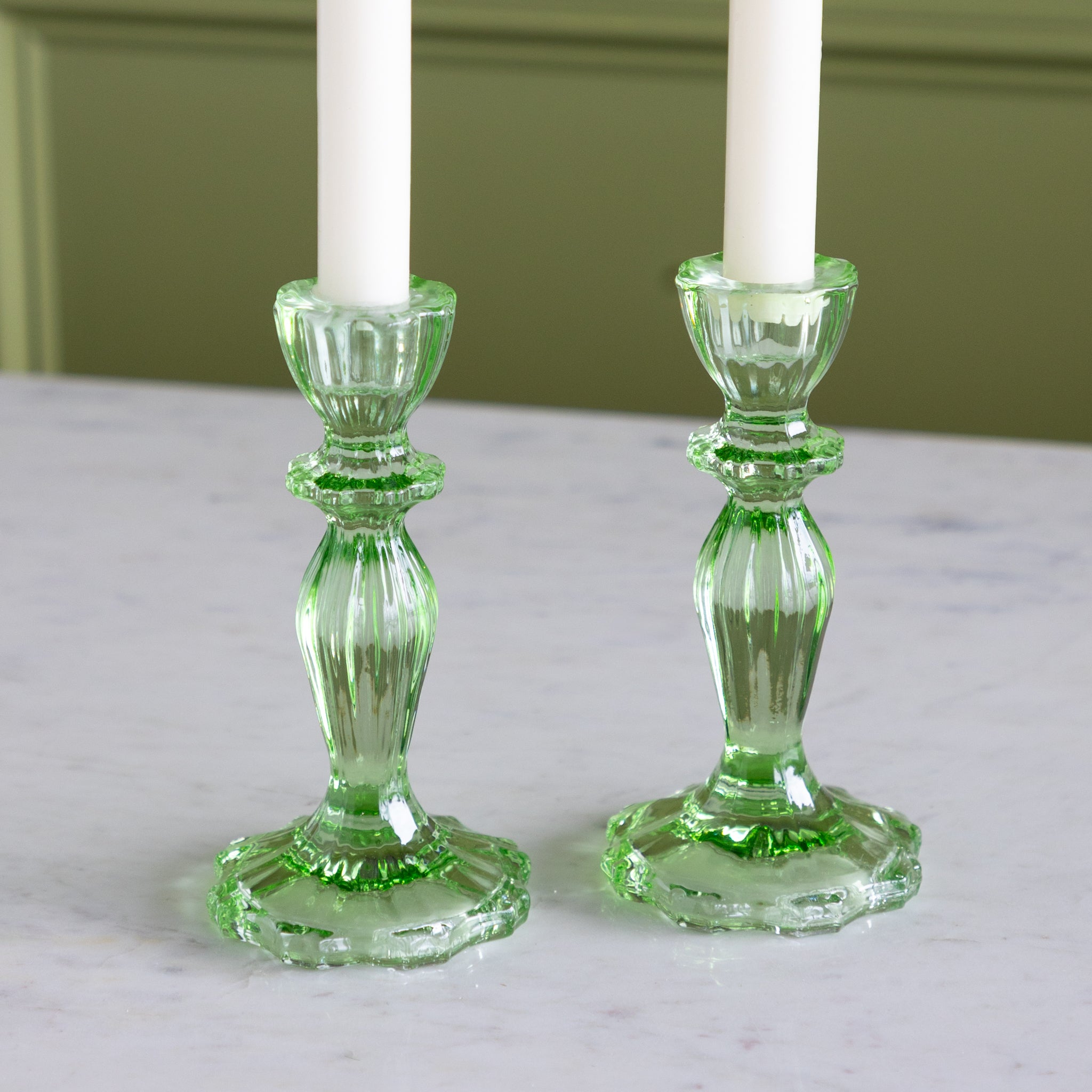 Pair of green glass candlesticks with white candles on a light surface.