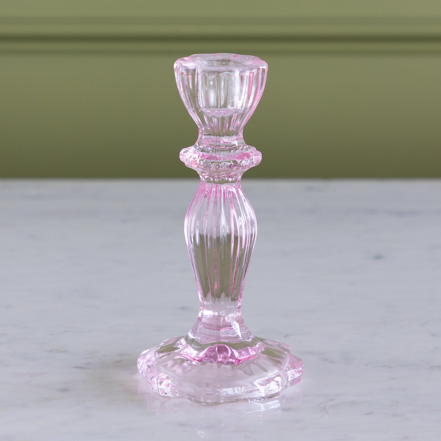 Pink glass candlestick holder on a marble surface with a green wall background.