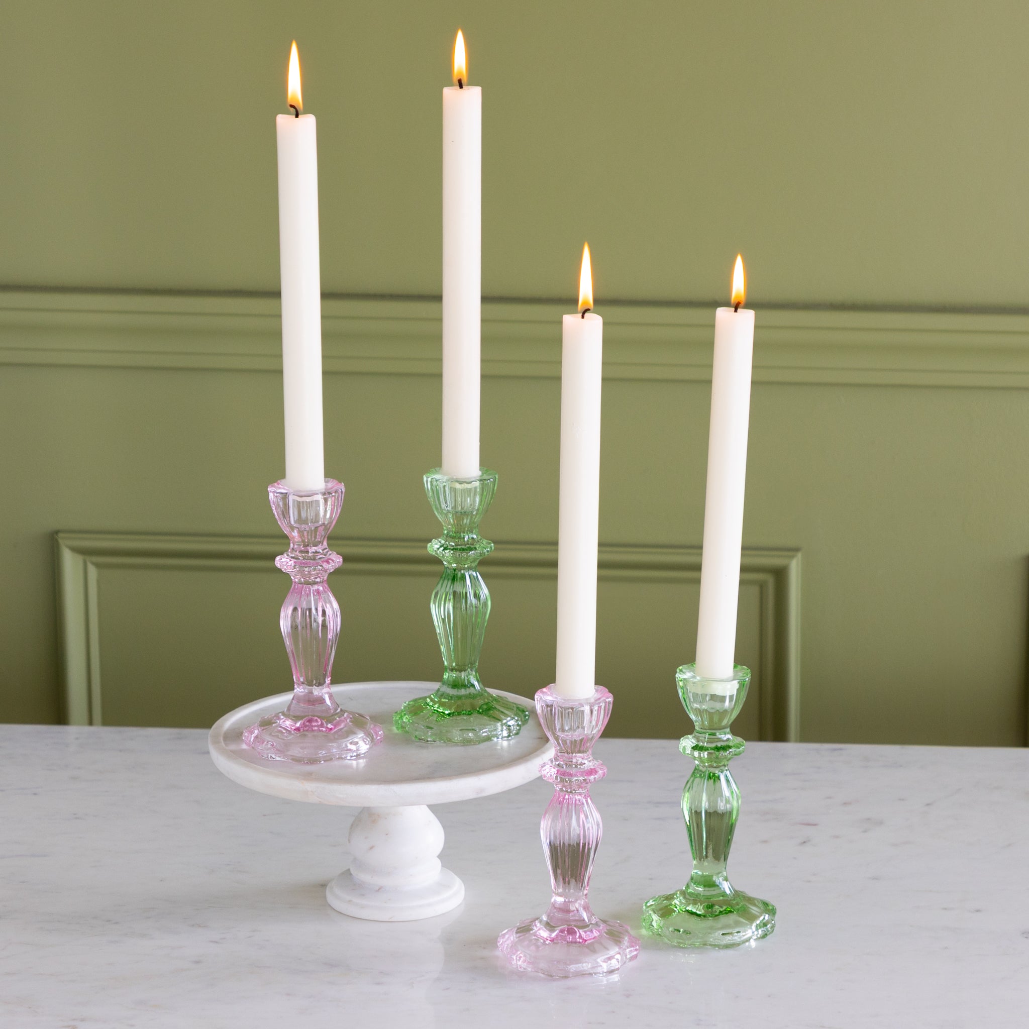 Four lit candles on decorative candlesticks against a green wall.