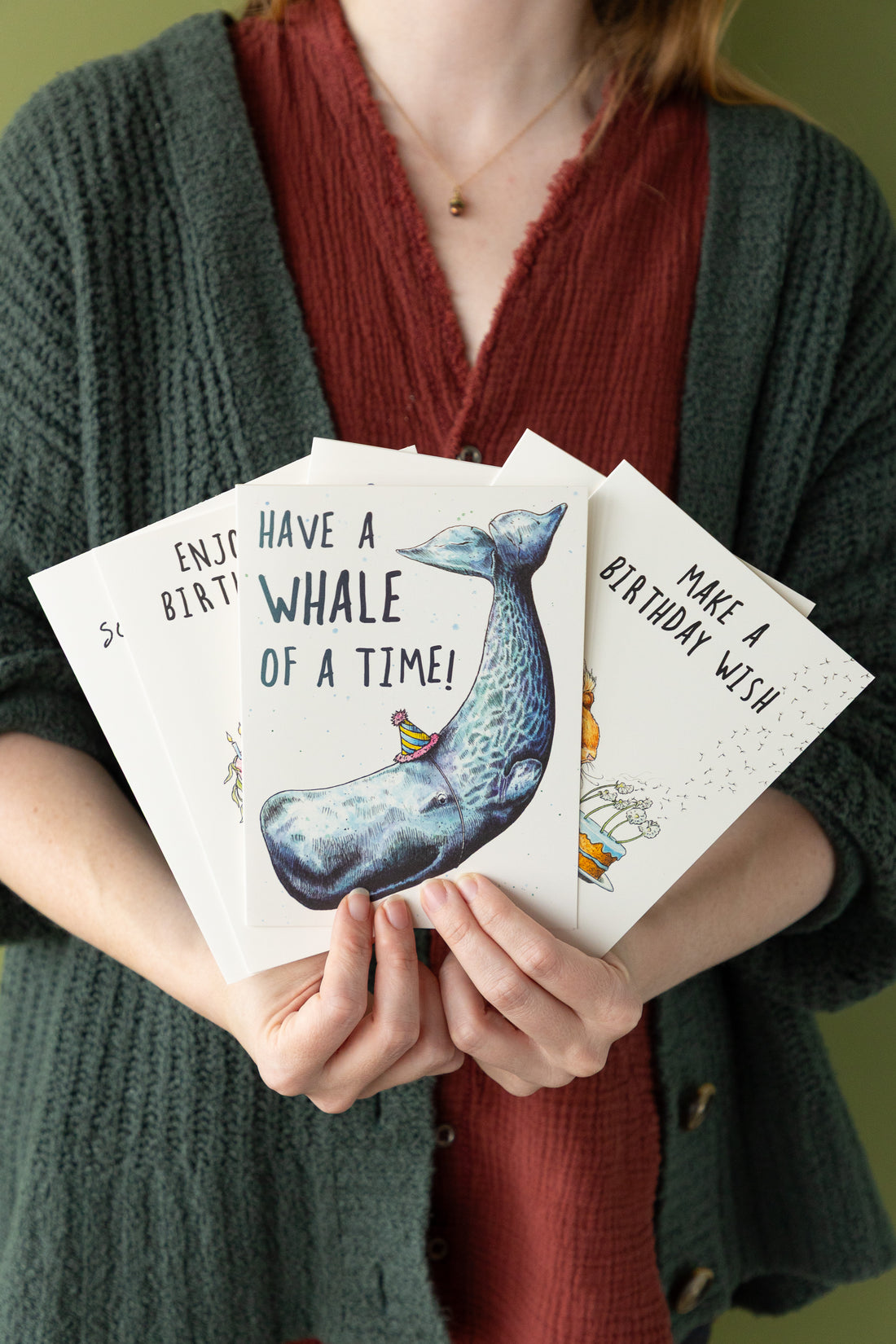 Person holding birthday cards with whale illustrations and text.