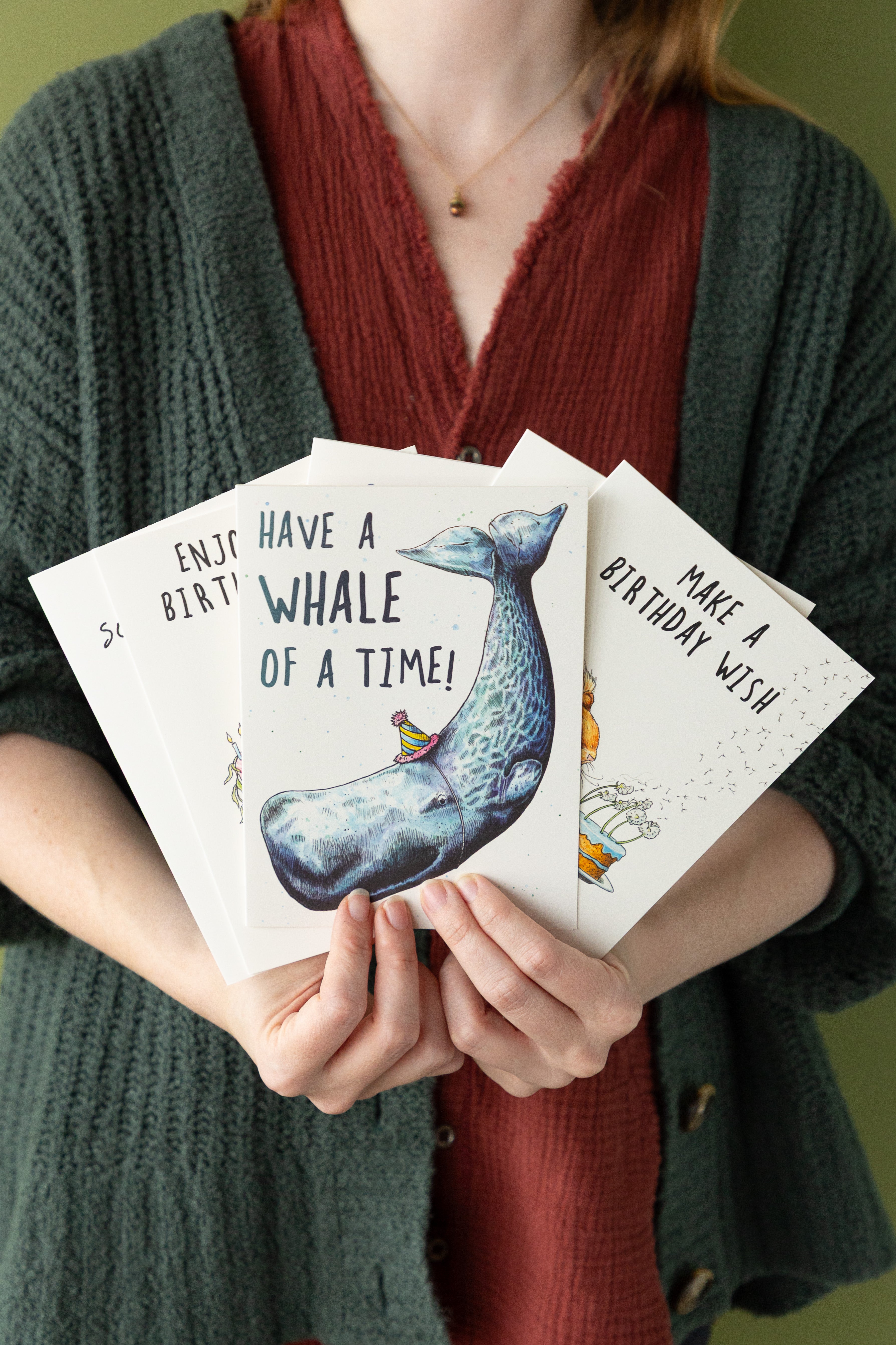 Person holding birthday cards with whale illustrations and text.